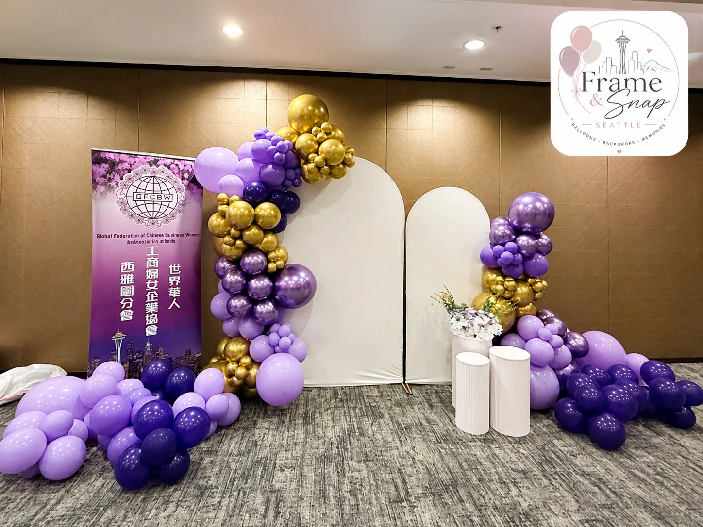 Lavender, violet and gold balloon garlands frame twin arch backdrops and fluted plinths for the Global Federation of Chinese Business Women Seattle chapter's presidential handover ceremony.