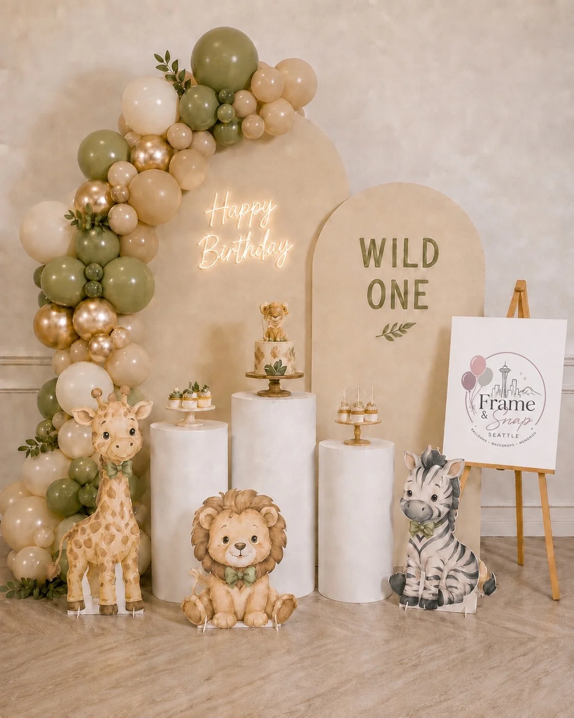 Olive, cream and gold balloons accompany safari animal illustrations, curved backdrops and white display plinths.