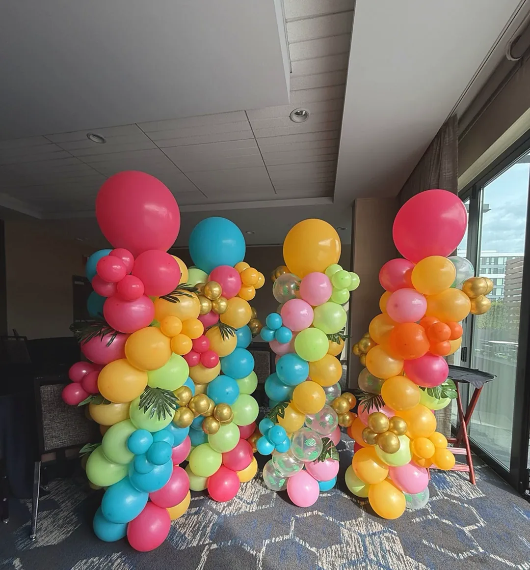 Bright tropical balloon columns in pink, orange, teal and gold, with an Aloha welcome table and a styled bar, for a Hilton client appreciation event.
